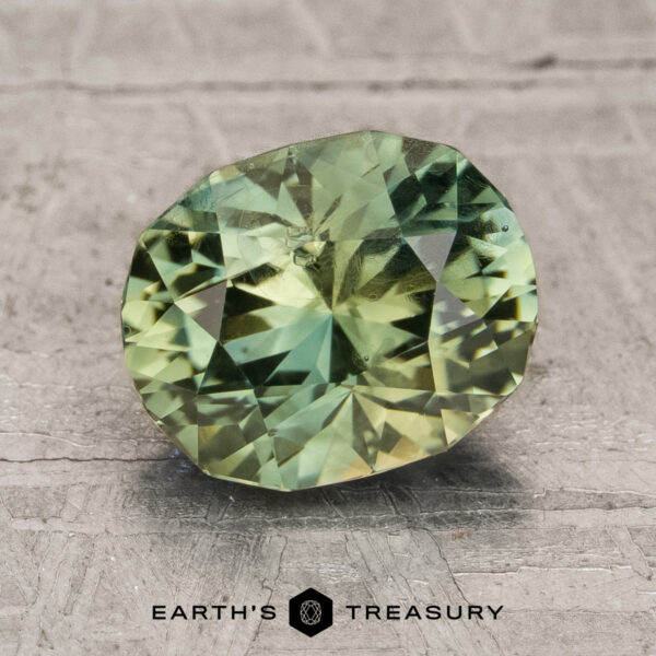 2.31-Carat Vietnam Sapphire (Unheated) A faceted, oval-shaped green 2.31-carat unheated Vietnam sapphire displayed on a textured gray surface with the text "EARTH'S TREASURY" below it.
