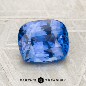 A 2.52-carat heated Ceylon sapphire with a cushion cut rests on a textured light gray surface, with the Earth's Treasury logo at the bottom.