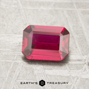 A 1.16-carat, rectangular emerald-cut ruby is displayed on a light, textured surface with the "Earth's Treasury" logo at the bottom.