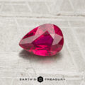 A 1.07-carat, pear-shaped faceted ruby rests on a textured, light surface with the text "EARTH'S TREASURY" below.