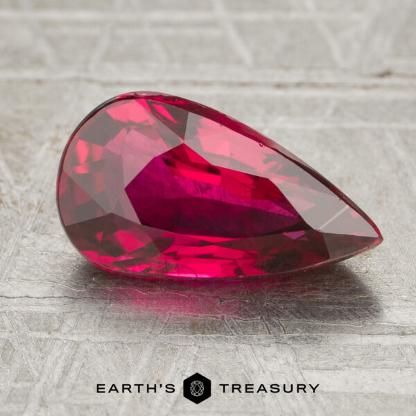2.23-Carat Ruby A 2.23-carat pear-shaped faceted ruby rests on a textured metallic surface with "Earth's Treasury" displayed below.