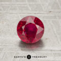 A 1.38-carat faceted round ruby is displayed on a textured surface with the text "EARTH'S TREASURY" beneath it.