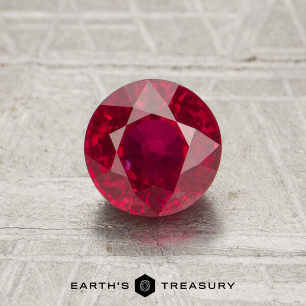 A 1.38-carat faceted round ruby is displayed on a textured surface with the text "EARTH'S TREASURY" beneath it.