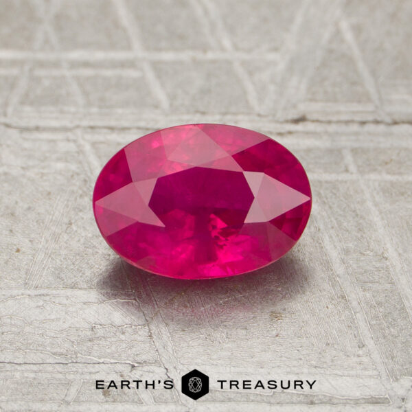 1.09-Carat Ruby A 1.09-carat oval-cut vivid pink ruby rests on a textured gray surface, with the "Earth's Treasury" logo below it.