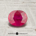 A 1.16-carat, oval-cut vivid red ruby rests on a textured light surface with "Earth's Treasury" below it.