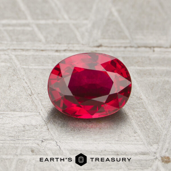 A 1.07-carat faceted oval ruby rests on a textured gray surface, with the "EARTH'S TREASURY" text and logo displayed below.