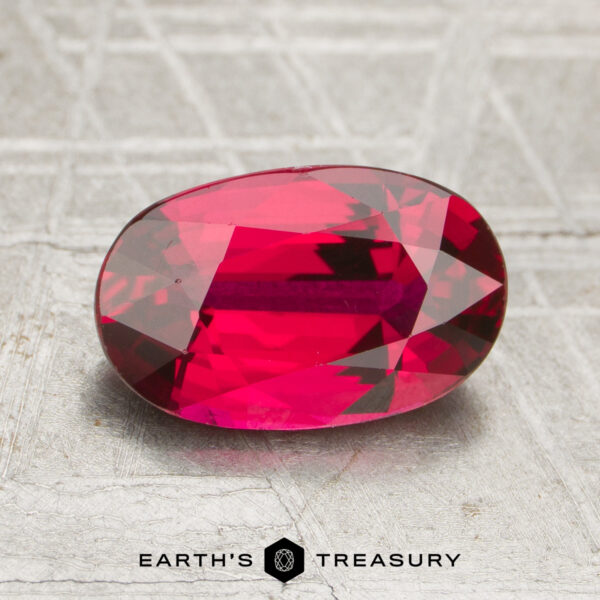 2.07-Carat Ruby A 2.07-carat oval-cut deep red ruby is displayed on a textured surface, with "EARTH'S TREASURY" written below the gemstone.