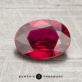 A 2.21-carat ruby with an oval faceted cut is displayed on a textured gray surface, with the text "EARTH'S TREASURY" below.
