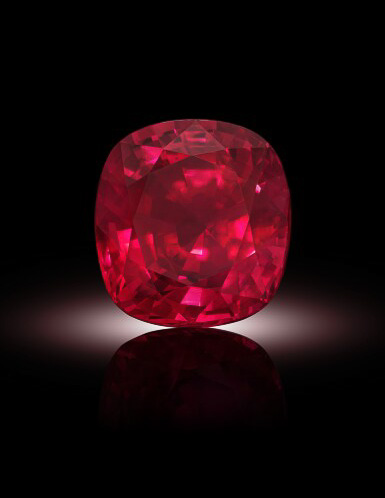 The download-1200-BW shows a cushion-cut, faceted red gemstone displayed against a black background with a subtle white spotlight beneath it.