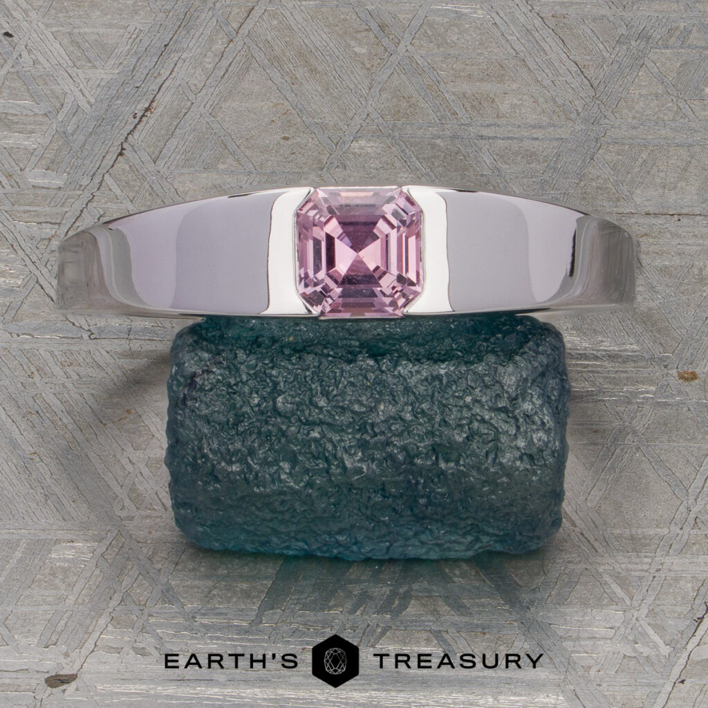 The "Wimmer, Janet 2" silver ring, featuring a rectangular pink gemstone, is displayed on a textured blue-green stone with the Earth's Treasury logo below.