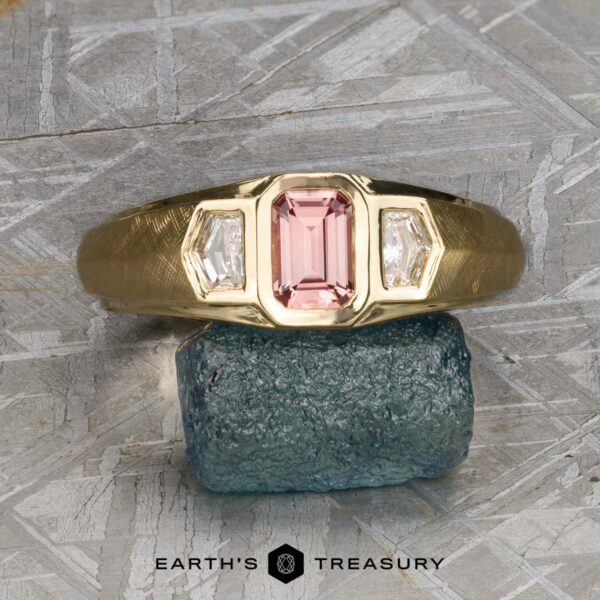 The "Firenze" ring in 18k yellow gold with 0.61-carat Montana sapphire The "Firenze" ring, expertly crafted in 18k yellow gold, features a 0.61-carat Montana sapphire center stone accented by two clear side stones. The ring is displayed on a rough blue-green mineral, with the "Earth's Treasury" text below.