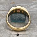 The "Firenze" ring, crafted in 18k yellow gold and featuring a 0.61-carat Montana sapphire, is displayed upside down to reveal its striking blue stone and a small inset gemstone. Resting on a patterned gray surface, this textured band ring is ready to ship.