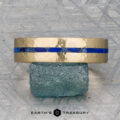 A "Stacked from 52 images. Method=B (R=14,S=2)" gold ring with a hammered finish and a striking blue inlay sits on a rough green stone, displayed on a textured gray surface with the "Earth's Treasury" logo below.