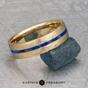 A gold ring from the "Stacked from 52 images. Method=B (R=14,S=2)" collection, featuring a striking blue inlay, rests on a rough, dark stone against a textured gray background. The text "EARTH'S TREASURY" appears at the bottom.