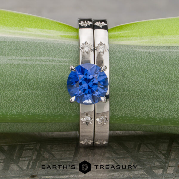 Stacked from 16 images. Method=B (R=7,S=2) Introducing Stacked from 16 images. Method=B (R=7, S=2): a round blue gemstone ring with two diamond-accented silver bands, elegantly displayed against a green and gray background.