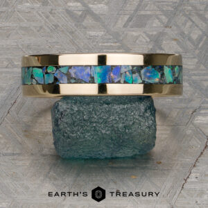 14K yellow gold ring with a band of blue-green opal inlay, displayed on a rough teal stone, with a geometric patterned background and "Earth's Treasury" logo at the bottom. This stunning "Stacked from 47 images. Method=B (R=7,S=2)" band is ready to ship.