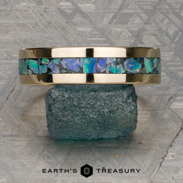 The "Triton" Ring 14K yellow gold ring with a band of blue-green opal inlay, displayed on a rough teal stone, with a geometric patterned background and "Earth's Treasury" logo at the bottom. This stunning "Stacked from 47 images. Method=B (R=7,S=2)" band is ready to ship.