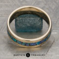 A stunning "Stacked from 49 images. Method=B (R=7,S=2)" band is displayed standing upright on a textured metallic surface, with a rough blue stone placed behind it. Ready to ship, this exquisite piece is showcased with the Earth’s Treasury logo at the bottom.