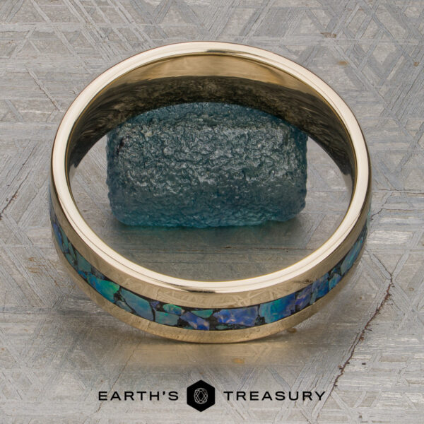 The "Triton" Ring A stunning "Stacked from 49 images. Method=B (R=7,S=2)" band is displayed standing upright on a textured metallic surface, with a rough blue stone placed behind it. Ready to ship, this exquisite piece is showcased with the Earth’s Treasury logo at the bottom.