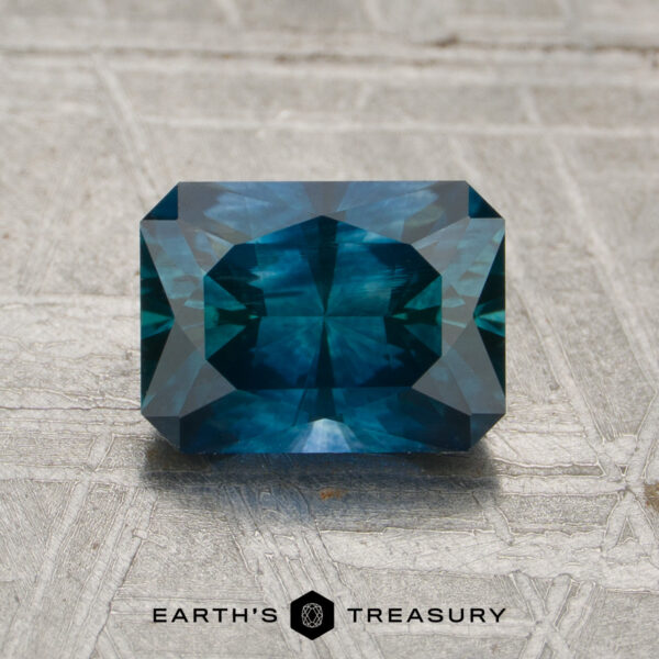 1.67-Carat Peacock Blue Montana Sapphire (Heated) A rectangular, faceted 1.67-carat Peacock Blue Montana Sapphire (Heated) rests on a textured gray surface with the "EARTH'S TREASURY" text and logo displayed below it.