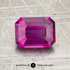 Rectangular emerald-cut 2.05-carat heated sapphire in bright pink, displayed on a textured metallic surface with the text "Earth's Treasury" at the bottom.