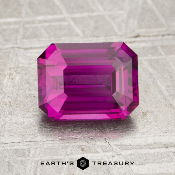 2.05-Carat Sapphire (Heated) Rectangular emerald-cut 2.05-carat heated sapphire in bright pink, displayed on a textured metallic surface with the text "Earth's Treasury" at the bottom.