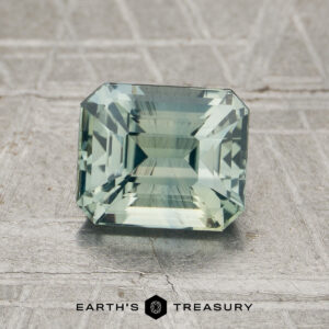 A 2.01-carat mint green Madagascar sapphire (heated), rectangular in shape and featuring step cuts, is displayed on a textured gray surface with the "Earth’s Treasury" logo visible at the bottom of the image.