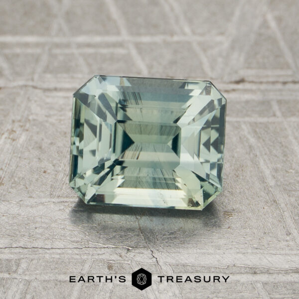 2.01-Carat Mint Green Madagascar Sapphire (Heated) A 2.01-carat mint green Madagascar sapphire (heated), rectangular in shape and featuring step cuts, is displayed on a textured gray surface with the "Earth’s Treasury" logo visible at the bottom of the image.