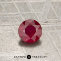 0.56-carat Mozambique Ruby (heated), round-cut, displayed on a textured gray surface with the "Earth's Treasury" logo and text at the bottom of the image.