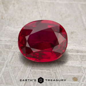 A 2.04-carat Mozambique ruby (heated), expertly cut in an oval shape, is displayed on a textured gray surface, with the "Earth's Treasury" logo and text at the bottom of the image.