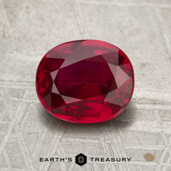 2.04-Carat Mozambique Ruby (Heated) A 2.04-carat Mozambique ruby (heated), expertly cut in an oval shape, is displayed on a textured gray surface, with the "Earth's Treasury" logo and text at the bottom of the image.