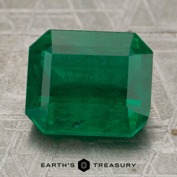 5.01-Carat Rich Green Zambian Emerald A 5.01-carat rich green Zambian emerald with step-cut facets is displayed on a textured surface, with the Earth's Treasury logo beneath it.