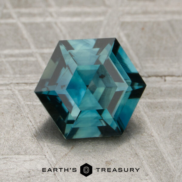 1.94-Carat Teal Madagascar Sapphire (Heated) A faceted, hexagonal 1.94-carat teal Madagascar sapphire (heated) rests on a textured surface with the Earth's Treasury logo and name at the bottom.