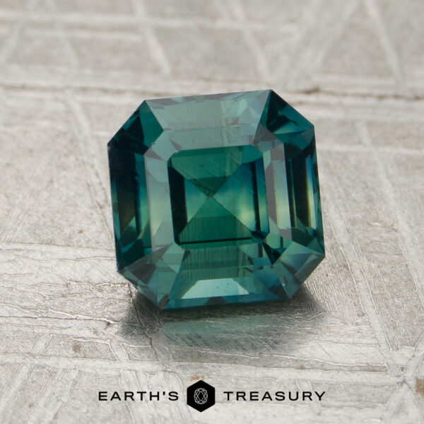 A 1.58-carat square-cut teal sapphire with emerald-style facets rests on textured silver. "EARTH'S TREASURY" is displayed at the bottom.