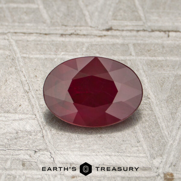 0.79-Carat Burmese Ruby (Heated) A 0.79-carat heated Burmese ruby, cut in a faceted oval shape, is displayed on a textured gray surface with the Earth's Treasury logo and text at the bottom of the image.