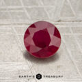A 0.77-carat heated Mozambique ruby, expertly faceted and round in shape, is displayed on a textured surface with the words "EARTH'S TREASURY" at the bottom.