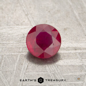 A 0.55-carat faceted red Mozambique ruby (heated) sits on a textured light surface with "EARTH'S TREASURY" at the bottom.