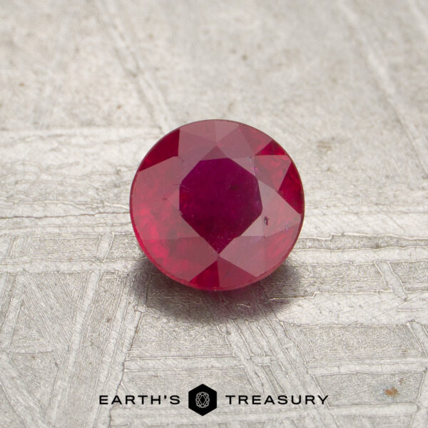 0.55-Carat Red Mozambique Ruby (Heated) A 0.55-carat faceted red Mozambique ruby (heated) sits on a textured light surface with "EARTH'S TREASURY" at the bottom.
