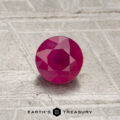 A 0.55-carat red Mozambique ruby (heated), round-cut, is displayed on a textured metallic surface with "EARTH'S TREASURY" and a hexagonal logo below.