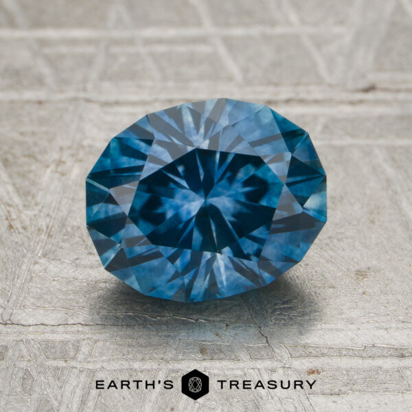 2.06-Carat Medium Blue Montana Sapphire (Heated) A 2.06-carat medium blue Montana sapphire (heated) rests on a textured gray surface, with the words "Earth's Treasury" and a hexagon logo displayed below it.