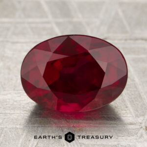 A 4.05-carat deep red Mozambique ruby (heated), cut in a faceted oval, displayed on a textured surface with the "EARTH'S TREASURY" logo and text below.
