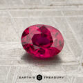 A 1.17-carat heated Mozambique ruby with an oval cut is displayed on a textured metallic surface, accompanied by the "EARTH'S TREASURY" text and a hexagonal logo below.