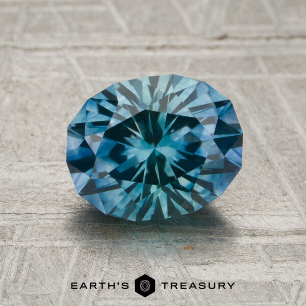 1.94-Carat Rich Aqua Blue Montana Sapphire (Heated) A 1.94-carat aqua-blue particolored Montana sapphire (heated) with intricate faceting is displayed on a textured gray surface, with the Earth’s Treasury logo below.