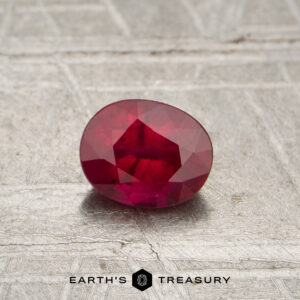 0.55-carat red Mozambique ruby (heated), oval-cut with visible inclusions, displayed on a textured surface above the text "EARTH'S TREASURY.