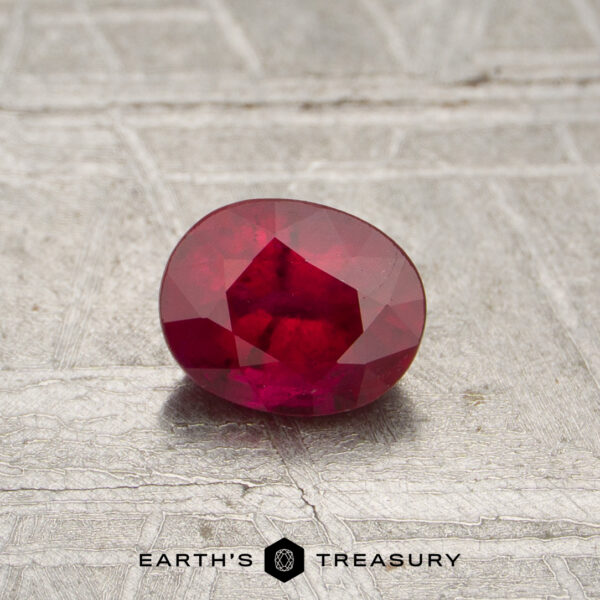 0.55-Carat Red Mozambique Ruby (Heated) 0.55-carat red Mozambique ruby (heated), oval-cut with visible inclusions, displayed on a textured surface above the text "EARTH'S TREASURY.