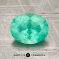 A 1.73-carat bright green Colombian emerald, oval-cut, is displayed on a textured metallic surface with the Earth’s Treasury logo at the bottom.