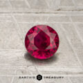A 0.66-carat round-cut red Mozambique ruby (heated) is displayed on a textured gray surface with the Earth's Treasury logo at the bottom.