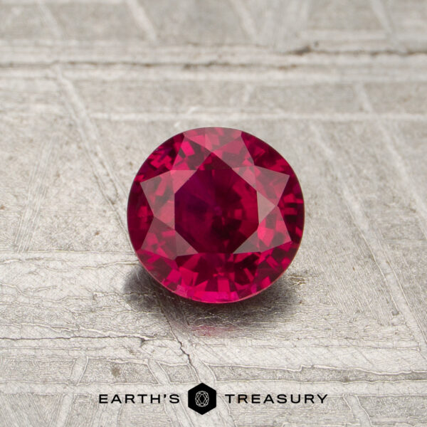 0.66-Carat Red Mozambique Ruby (Heated) A 0.66-carat round-cut red Mozambique ruby (heated) is displayed on a textured gray surface with the Earth's Treasury logo at the bottom.