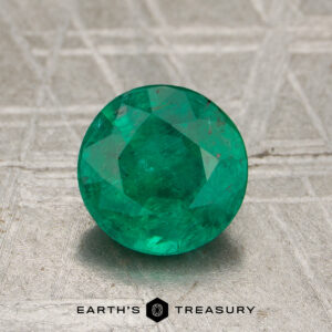 1.04-Carat Emerald gemstone, round faceted and green, shown on a metallic background with "Earth's Treasury" text and logo at the bottom.