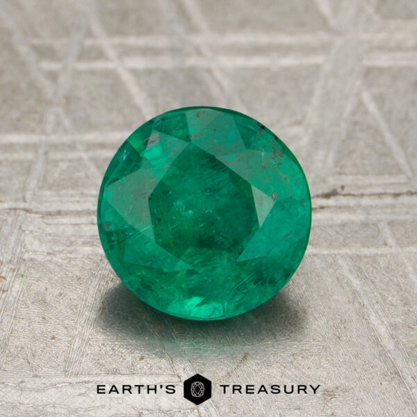 1.04-Carat Emerald 1.04-Carat Emerald gemstone, round faceted and green, shown on a metallic background with "Earth's Treasury" text and logo at the bottom.